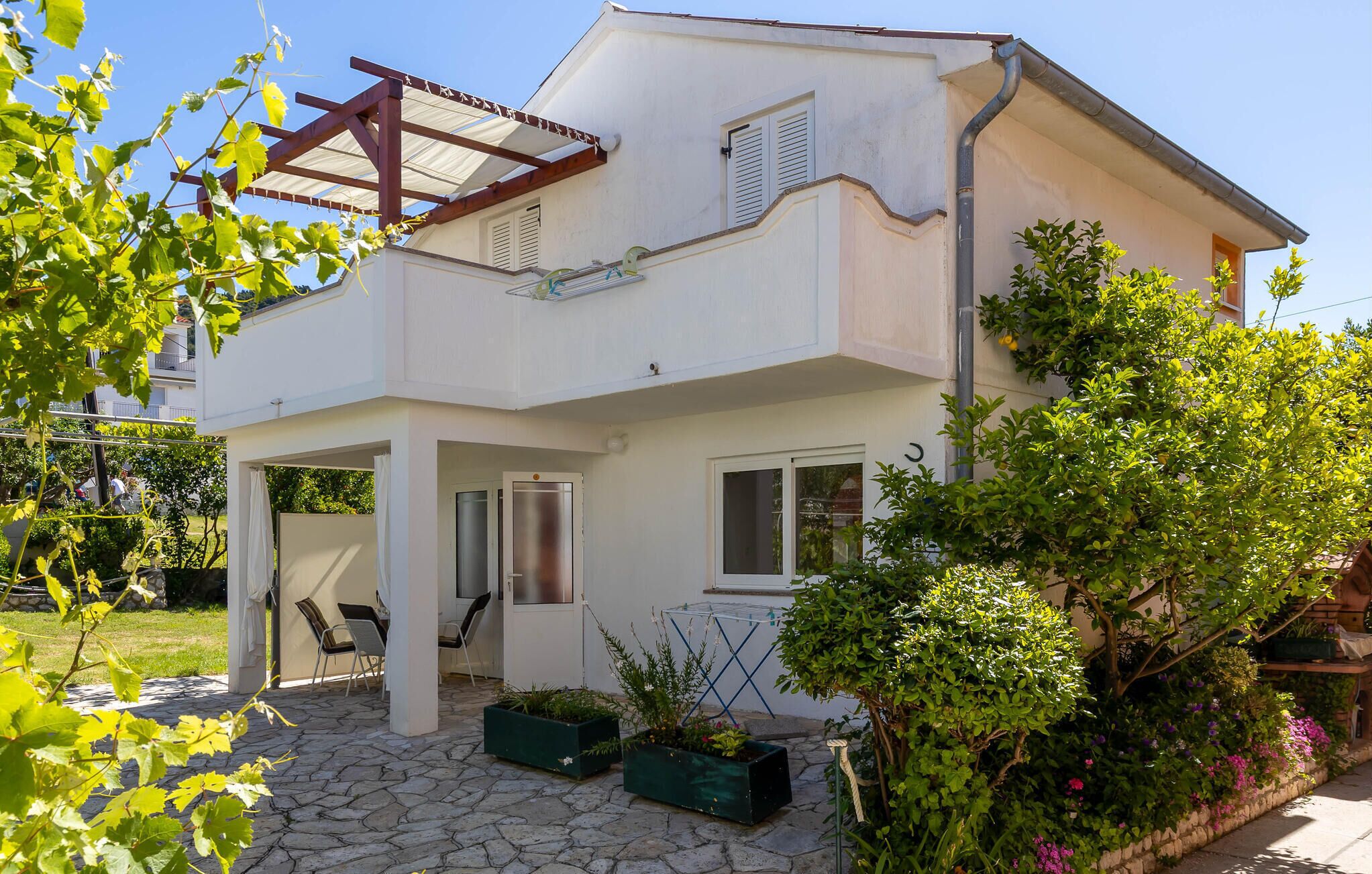 Uma casa de dois andares com varanda coberta, área de estar externa e um jardim.