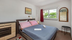A bedroom with a bed, bedside table, lamp, window with curtains, and a mirror.
