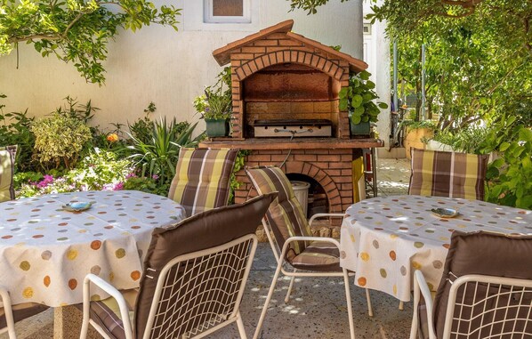 An outdoor patio with a brick pizza oven, two round tables with polka dot tablecloths, and metal chairs.