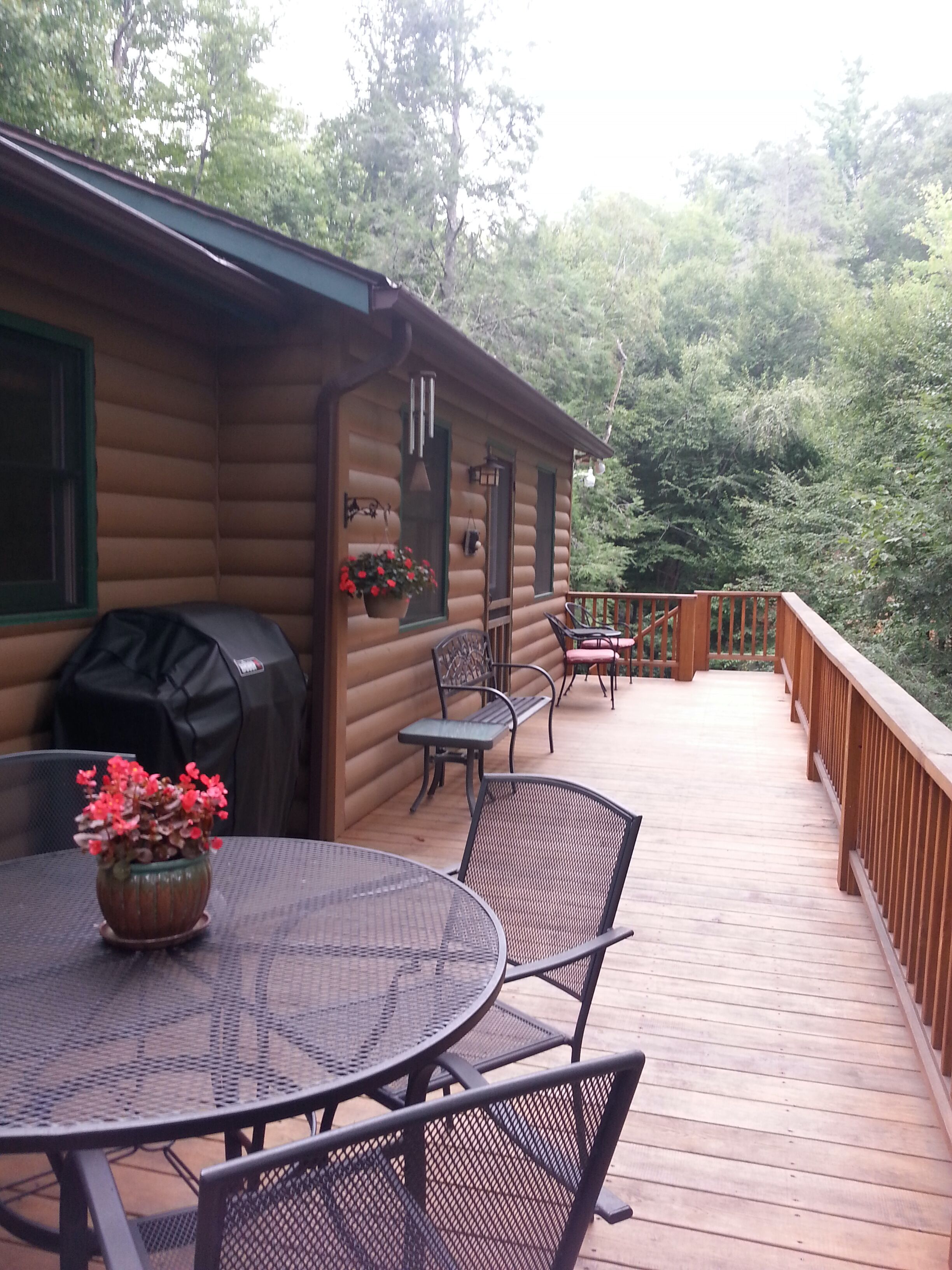A wooden deck with a round table and chairs, a barbecue grill, and potted plants.