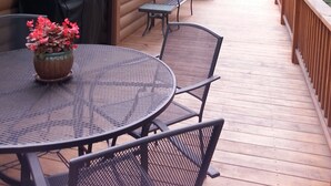 Una terraza de madera con una mesa redonda y sillas, una parrilla y plantas en macetas.