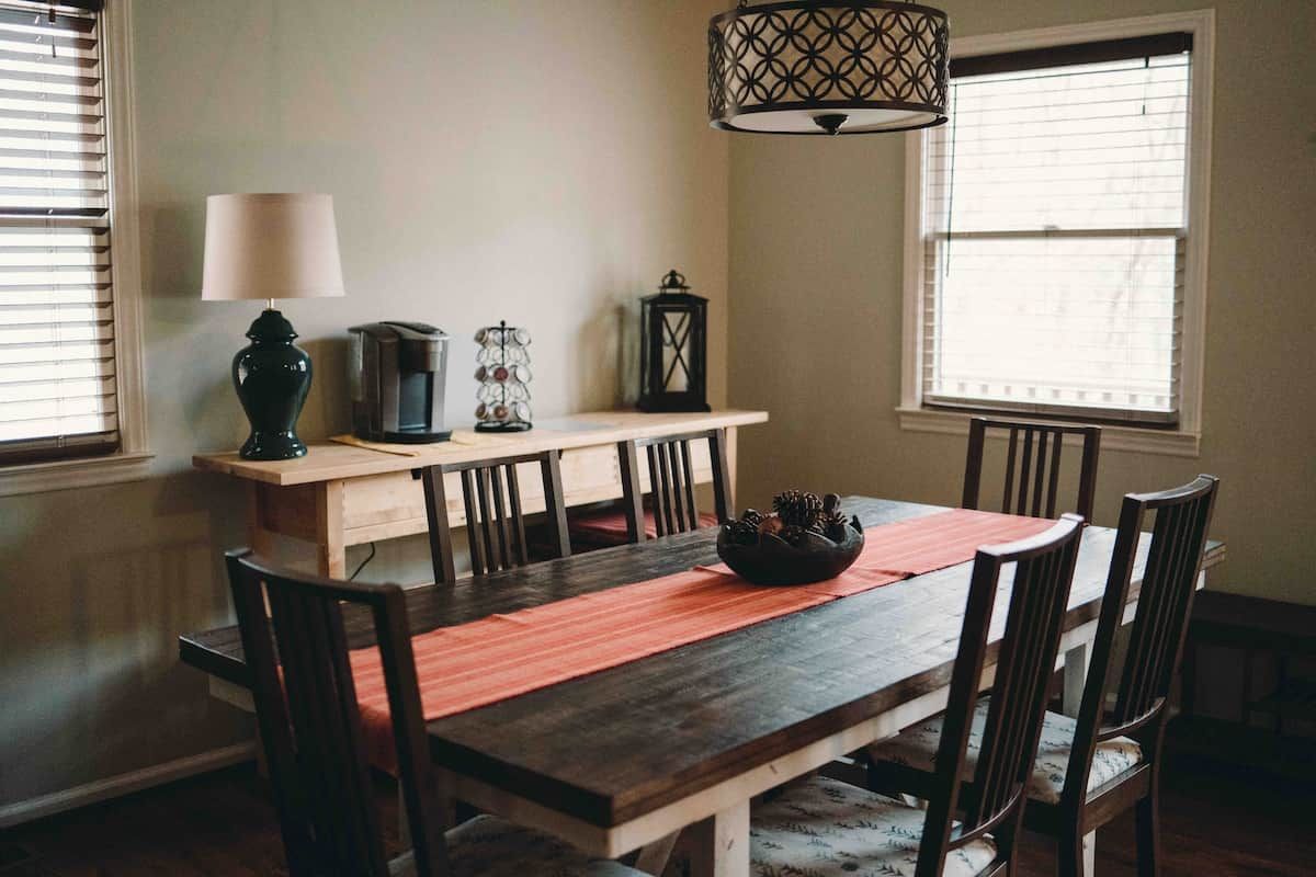Un coin repas comprenant une table en bois, des chaises, un banc, une lampe et un luminaire suspendu.