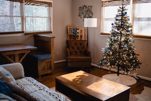Un salon chaleureux avec une table basse en bois, un fauteuil en cuir marron et un sapin de Noël décoré d’ornements bleus et argentés.