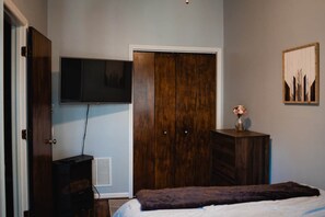 A bedroom with a bed, a wardrobe, a television, and a small table with a vase.