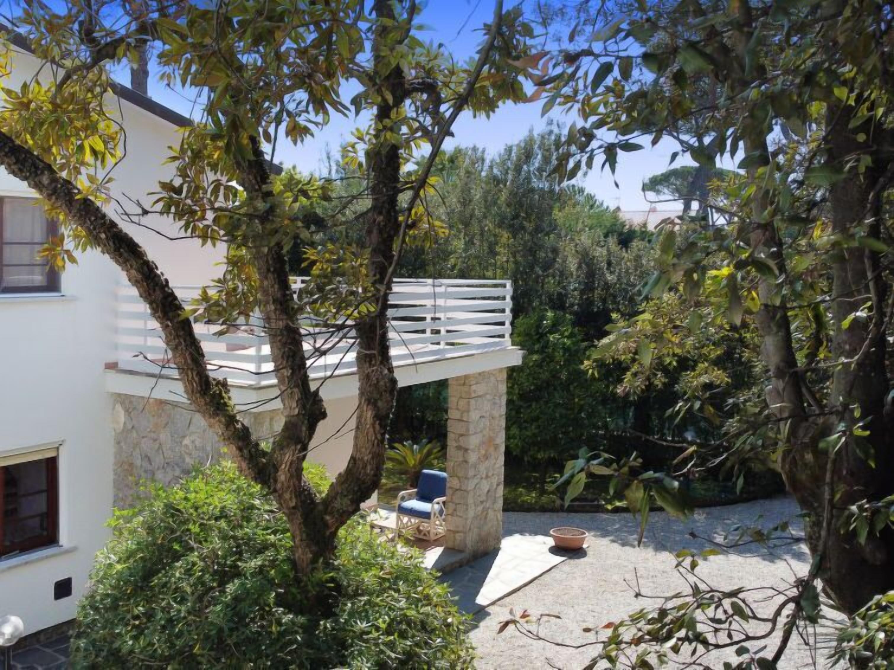 Ein modernes Haus mit Steinfundament, einem weißen Balkon und üppiger Vegetation ringsum.