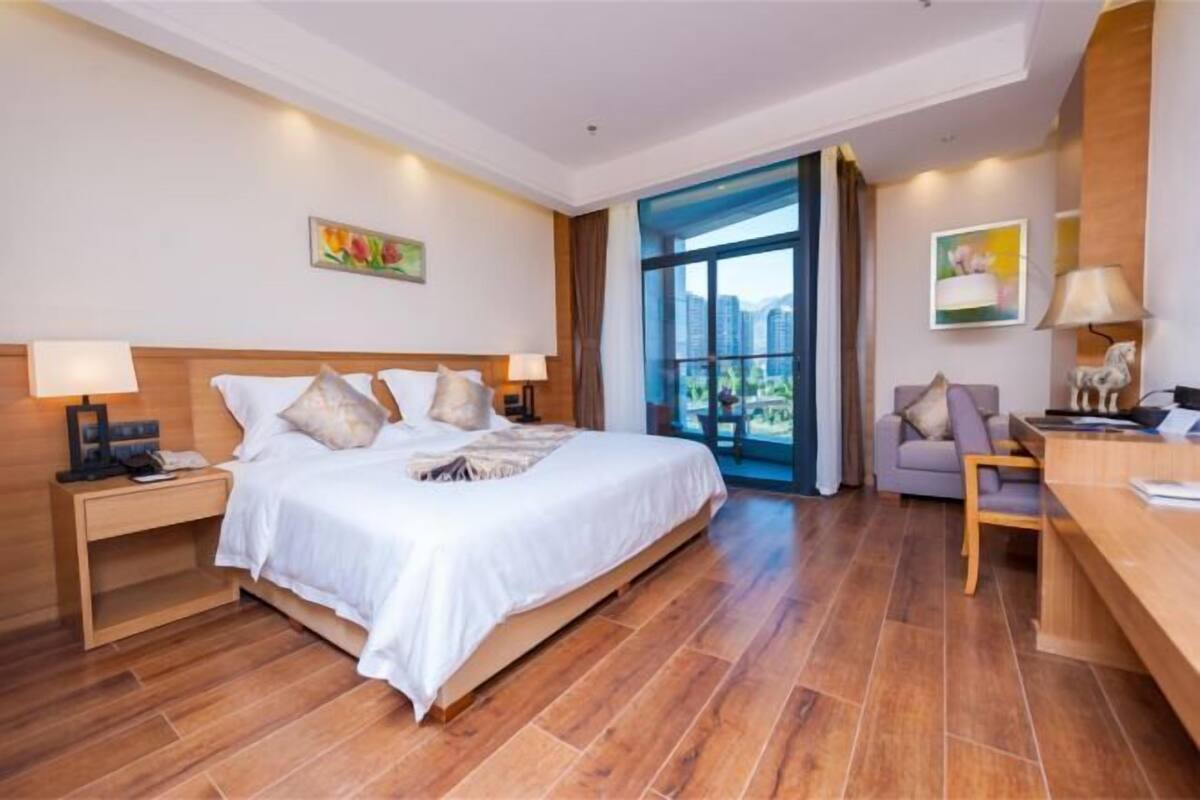 A hotel room with a bed, bedside tables, a desk, and a view of the outdoors.