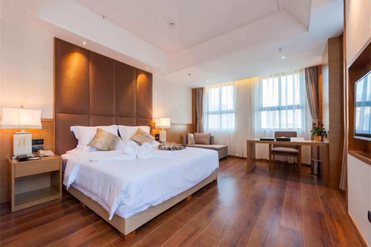 A spacious hotel room with a large bed, bedside tables, a desk, and a chair.
