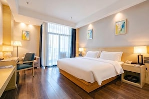A hotel room with a large bed, bedside tables, a desk, a chair, and a window with curtains.