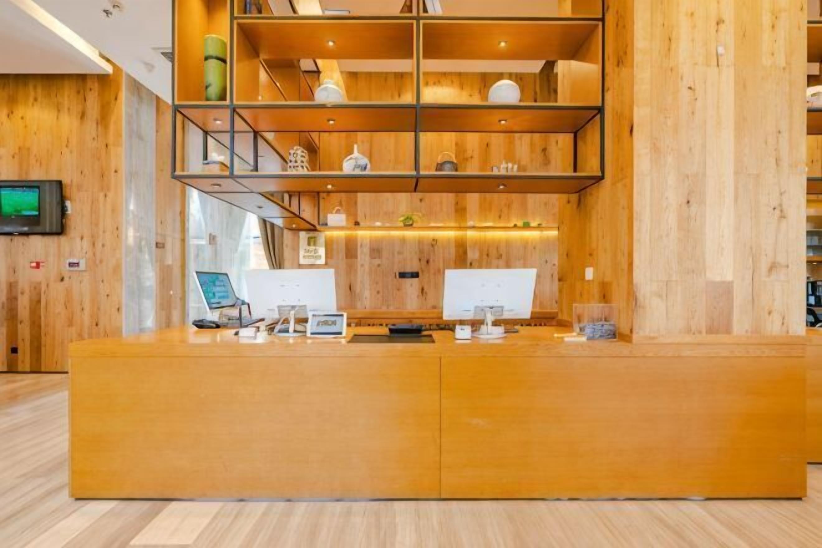 A reception desk with a wooden finish, two computer monitors, and a shelf with decorative items.
