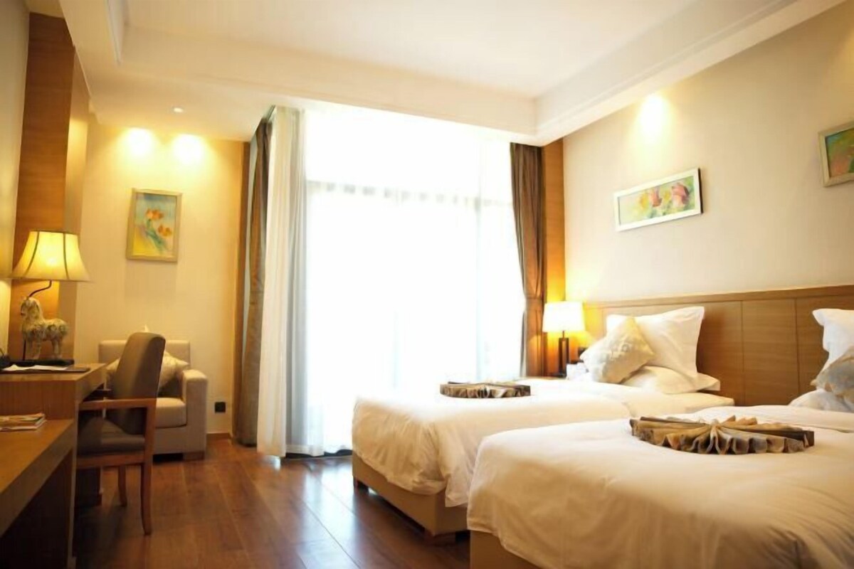 Habitación de hotel con dos camas, un escritorio, una silla y una ventana con cortinas.