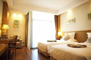 Habitación de hotel con dos camas, un escritorio, una silla y una ventana con cortinas.