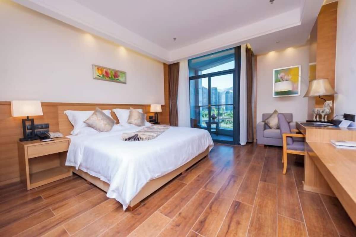 A hotel room with a large bed, a desk, a chair, and a view of the outdoors.