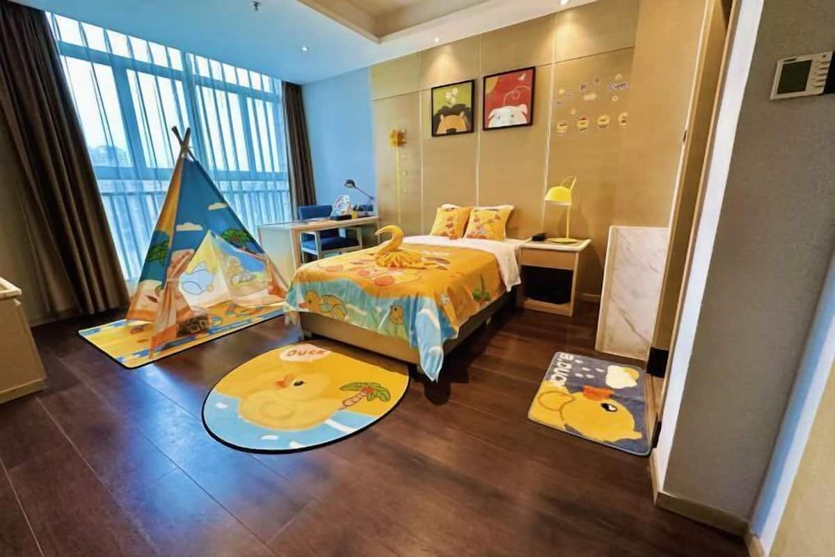 A hotel room with a bed, a desk, a chair, a nightstand, a lamp, and a window with curtains.
