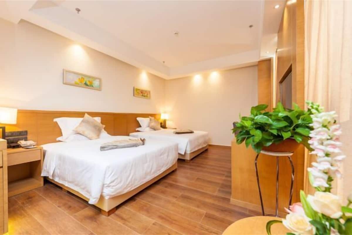 A hotel room with two beds, wooden flooring, and a potted plant.