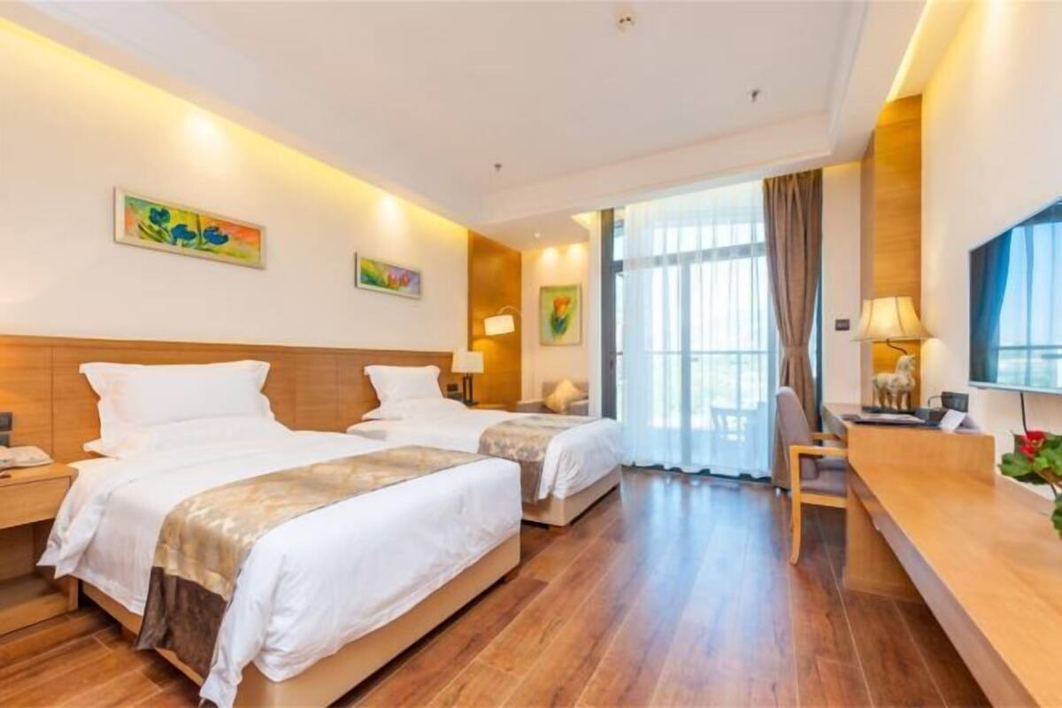 A hotel room with two beds, a desk, and a large window.