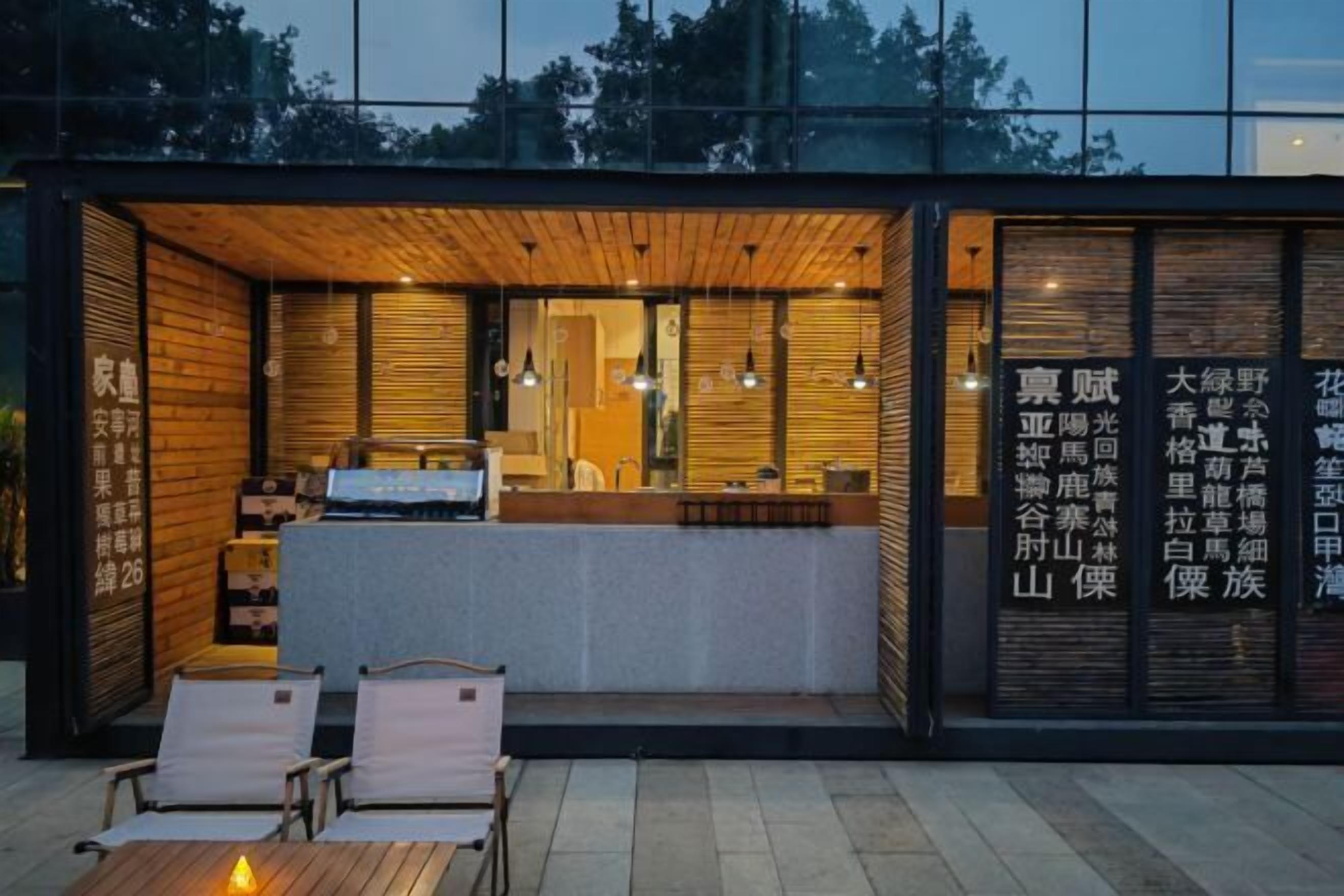 Een modern gebouw met een houten gevel en grote ramen. Binnenin bevindt zich een receptiebalie en een zitgedeelte.