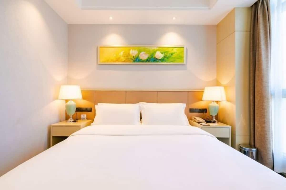 A hotel room with a large bed, two bedside tables with lamps, a painting on the wall, and a window with curtains.