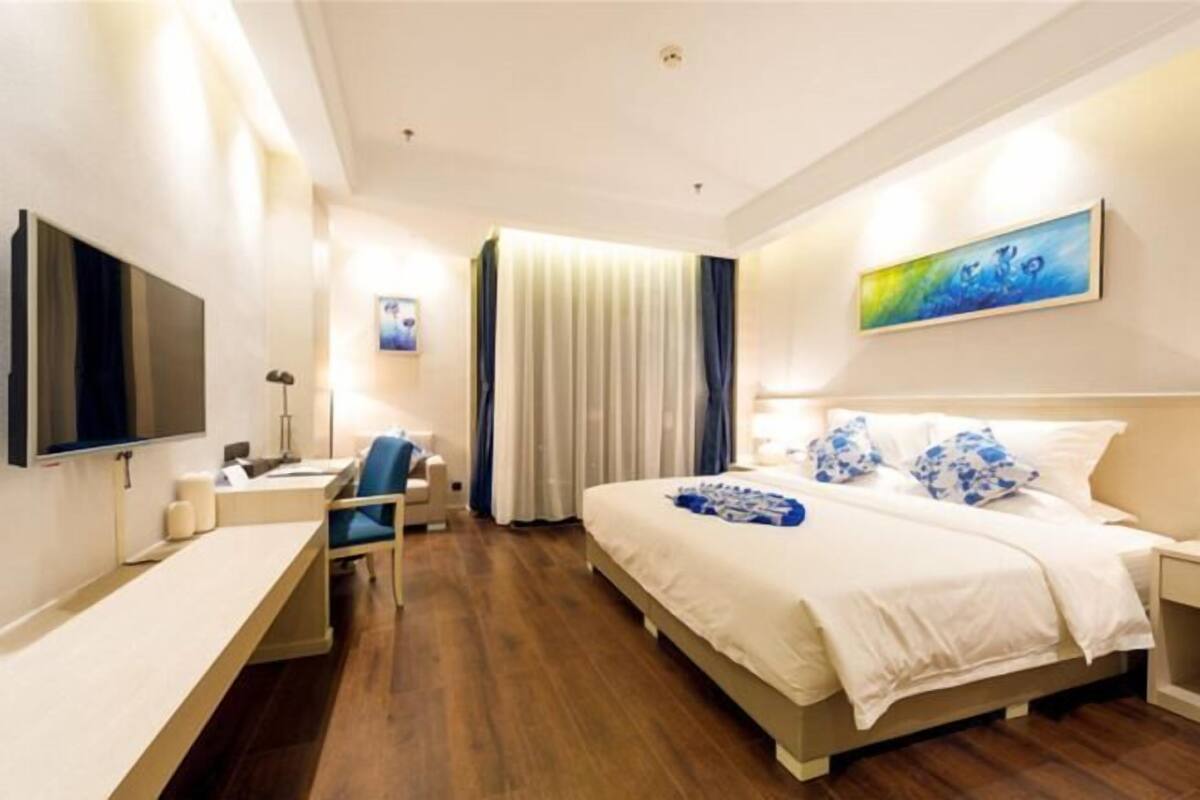 A hotel room with a bed, a desk, a chair, a TV, and a painting on the wall.