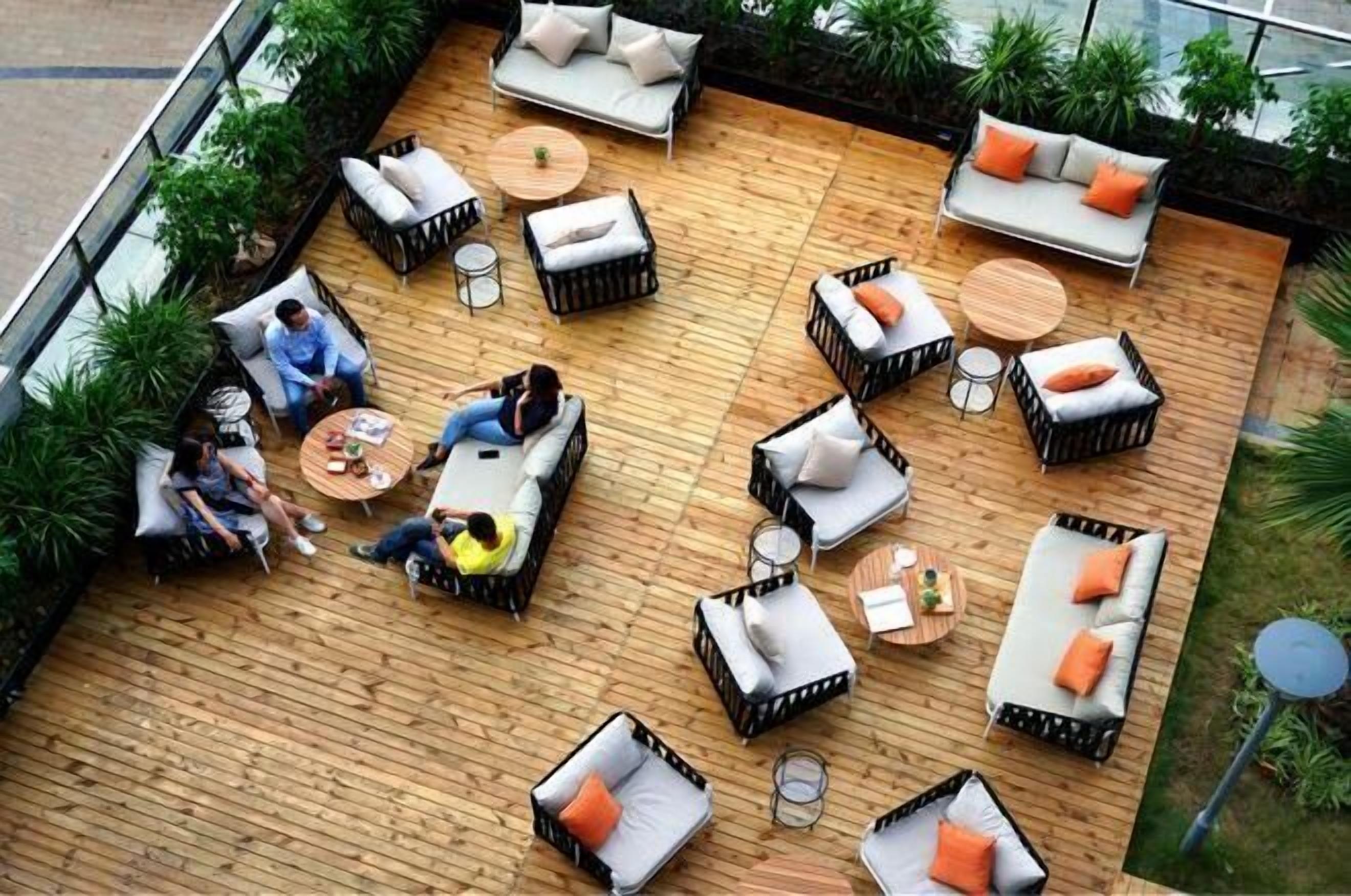 Een terras buiten met verschillende zithoeken, waaronder banken en stoelen, omringd door groen.