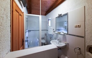 A bathroom with a wooden door, a shower, a toilet, a sink, and a mirror.