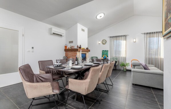A modern dining area with a long table set for six, surrounded by cushioned chairs. - Luxurious home in Sosici (Sosici)