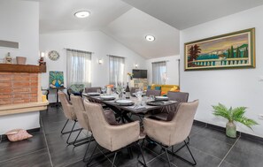 Un coin repas agrémenté d’une cheminée en briques, une table à manger dressée pour six personnes et un téléviseur en arrière-plan.