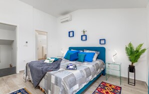 Une chambre à coucher moderne avec une tête de lit bleue, une couvre-lit à motifs et une petite table de chevet avec une lampe.