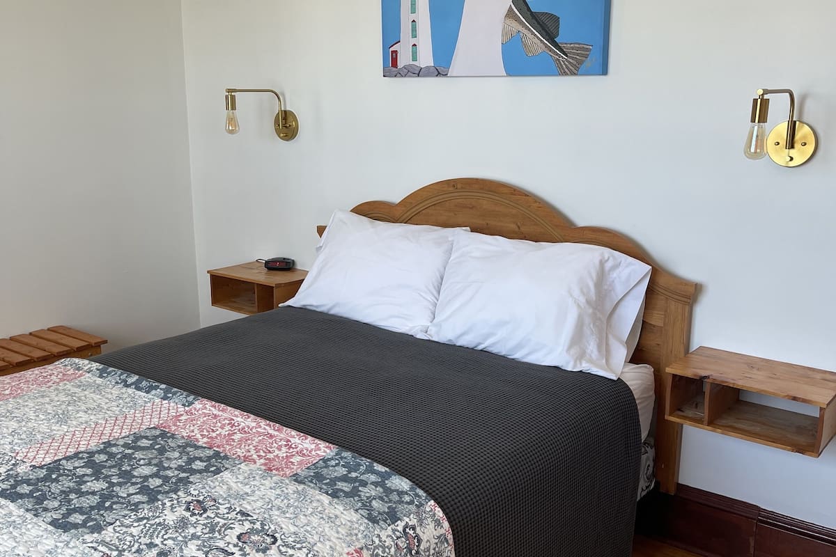 Ein Schlafzimmer mit einem Bett, einem Nachttisch, einer Wandleuchte und einem Gemälde.