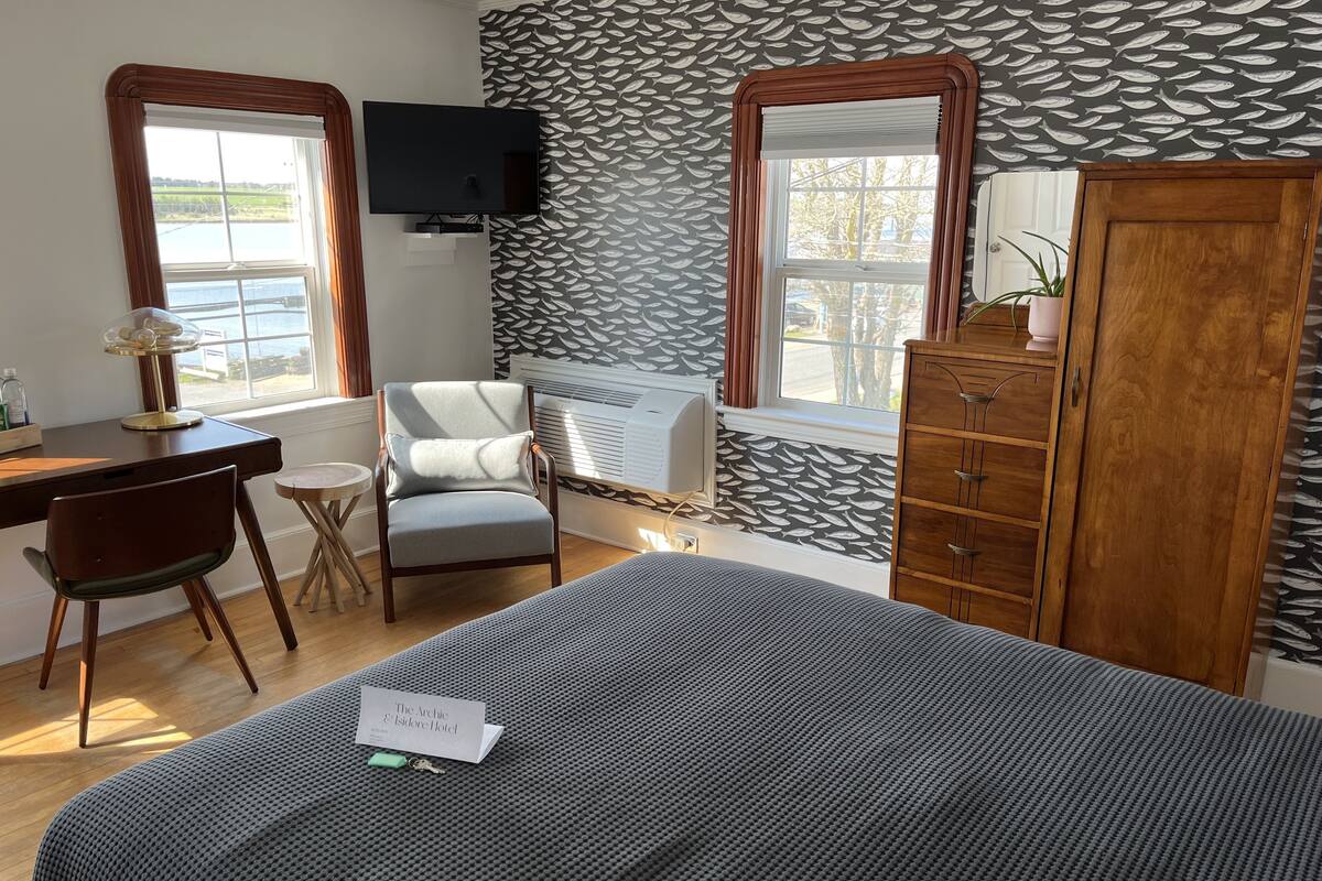 Ein Hotelzimmer mit Bett, Schreibtisch, Stuhl, Kleiderschrank und Fernseher.