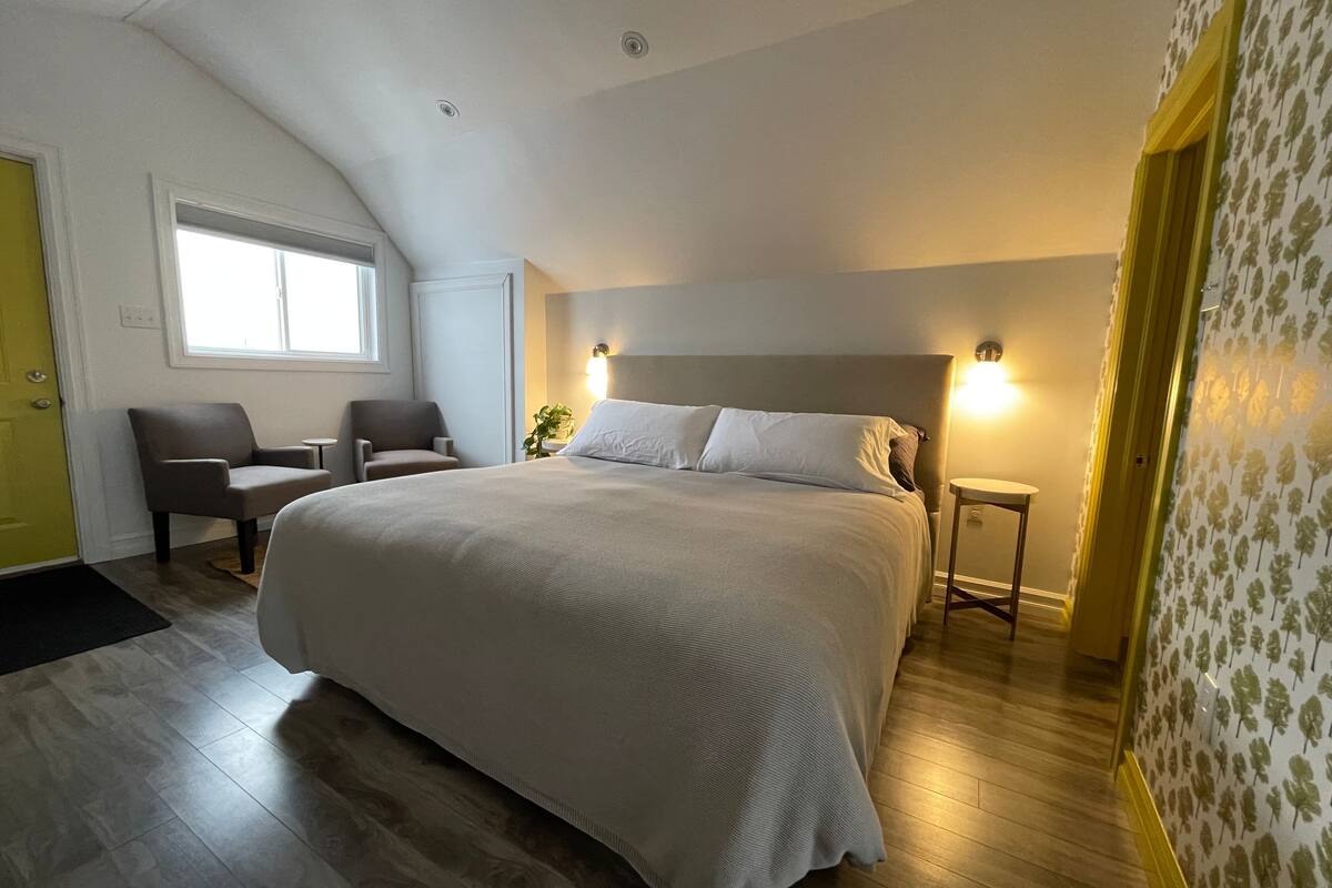 Ein Schlafzimmer mit einem großen Bett, zwei Stühlen, einem Nachttisch, einem Fenster und einer Tür.