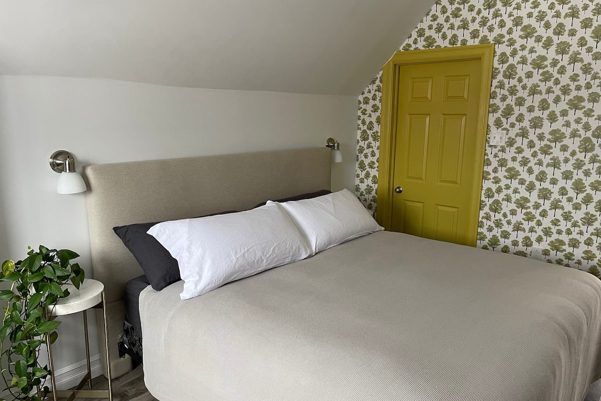 Ein Schlafzimmer mit einem Bett, einer Nachttischlampe, einem Blumentopf und einer Tür mit Tapete mit Baummuster.