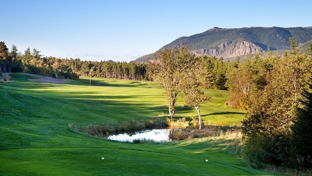 Un campo de golf con un estanque, árboles y una montaña al fondo.