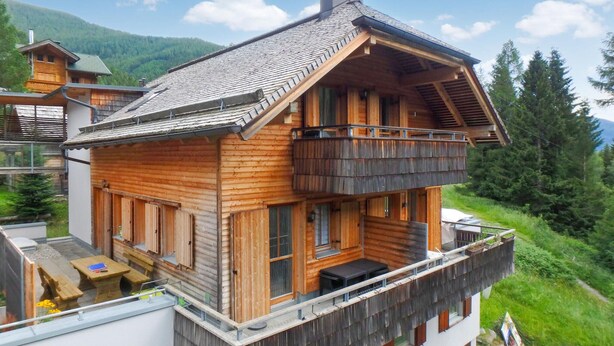 Una cabaña de madera con balcón, ventanas grandes y techo inclinado.