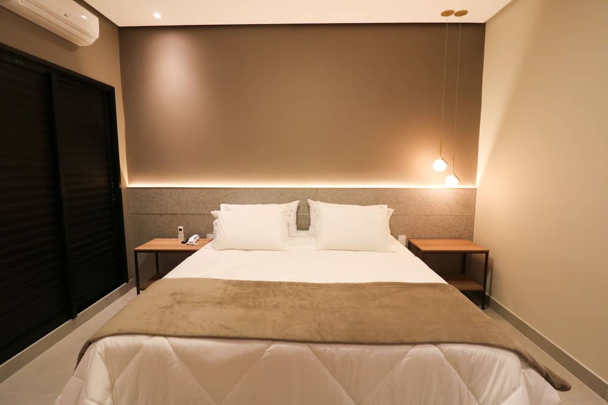 Ein Hotelzimmer mit einem großen Bett, zwei Nachttischen, einer Wandklimaanlage und einer Deckenleuchte.