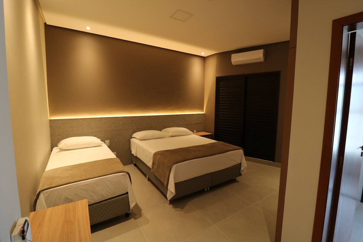 Ein Hotelzimmer mit zwei Betten, einem Nachttisch, einer Wand-Klimaanlage und einer Tür.