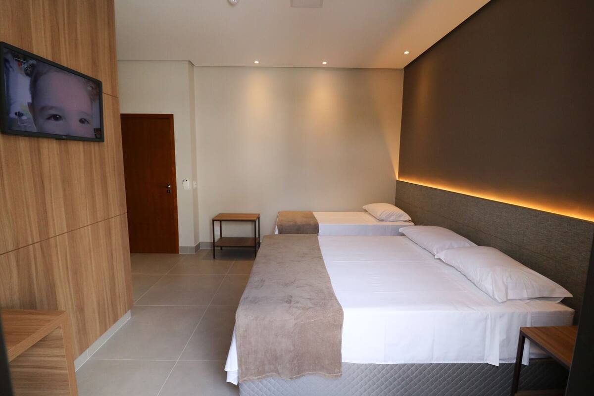 Ein modernes Hotelzimmer mit einem großen Bett, einem kleinen Nachttisch, einem an der Wand montierten Fernseher und einer Holzvertäfelung an einer Seite.