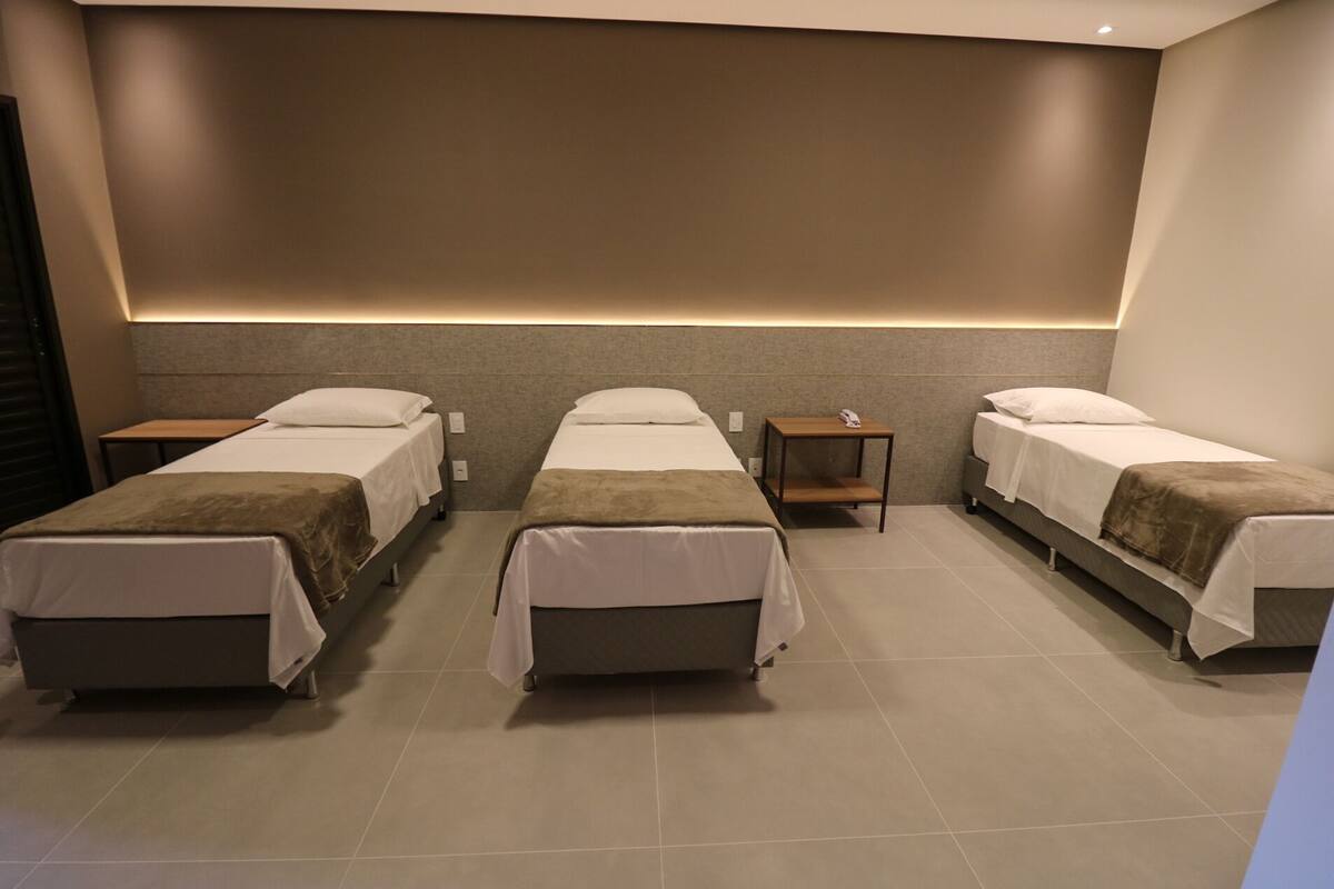 Ein Hotelzimmer mit drei Einzelbetten, einem kleinen Tisch und einem Nachttisch.
