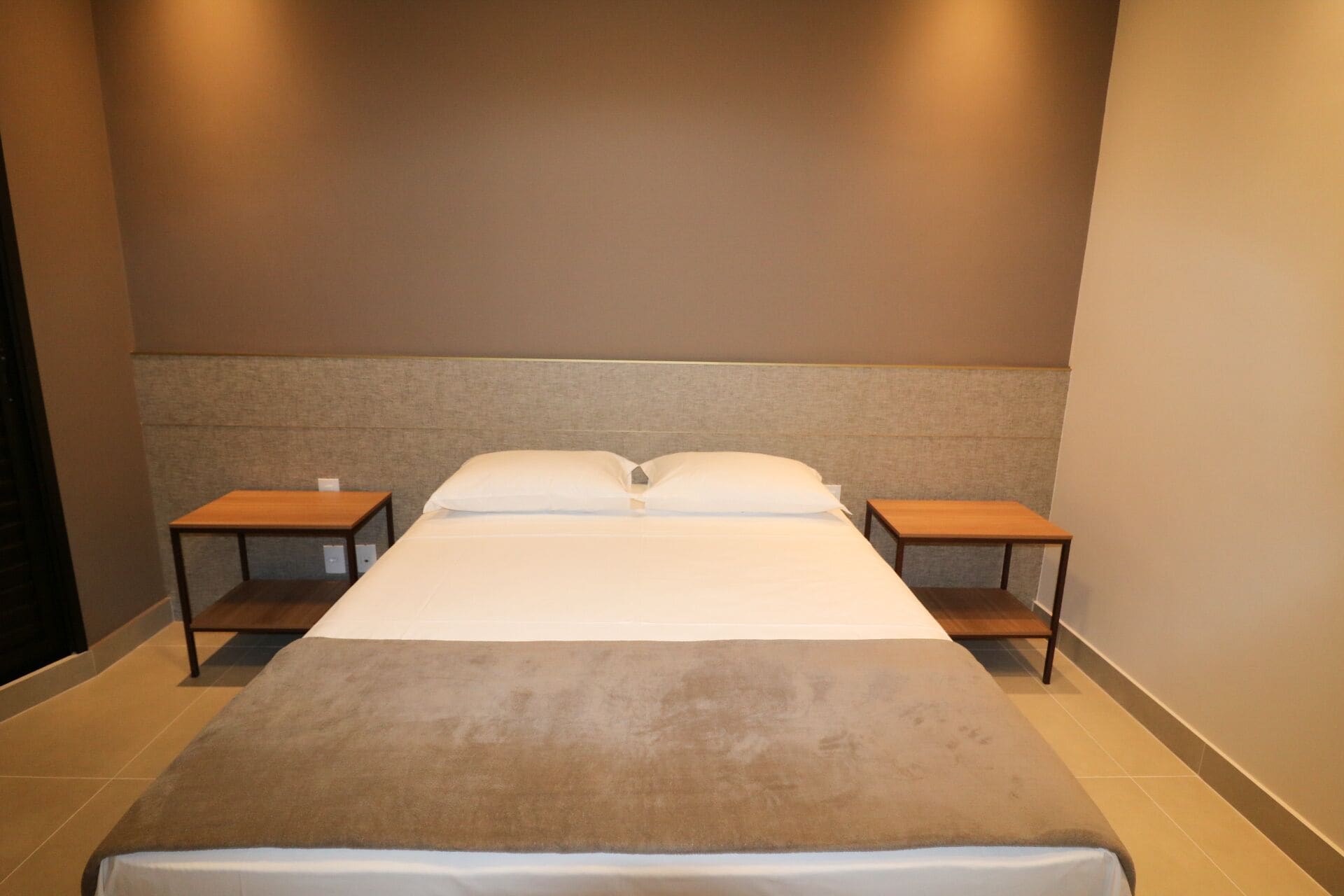 Une chambre d’hôtel avec un grand lit, deux tables de chevet et une tête de lit.
