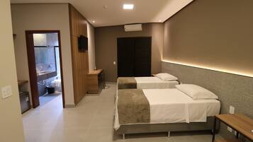 A hotel room with two beds, a desk, a TV, and a bathroom visible through an open door.