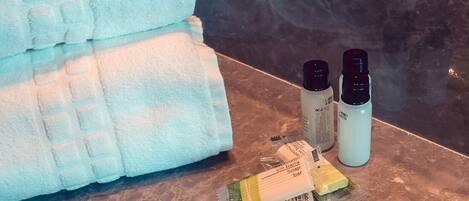 Un baño con una toalla, jabón y botellas de champú sobre el mostrador.