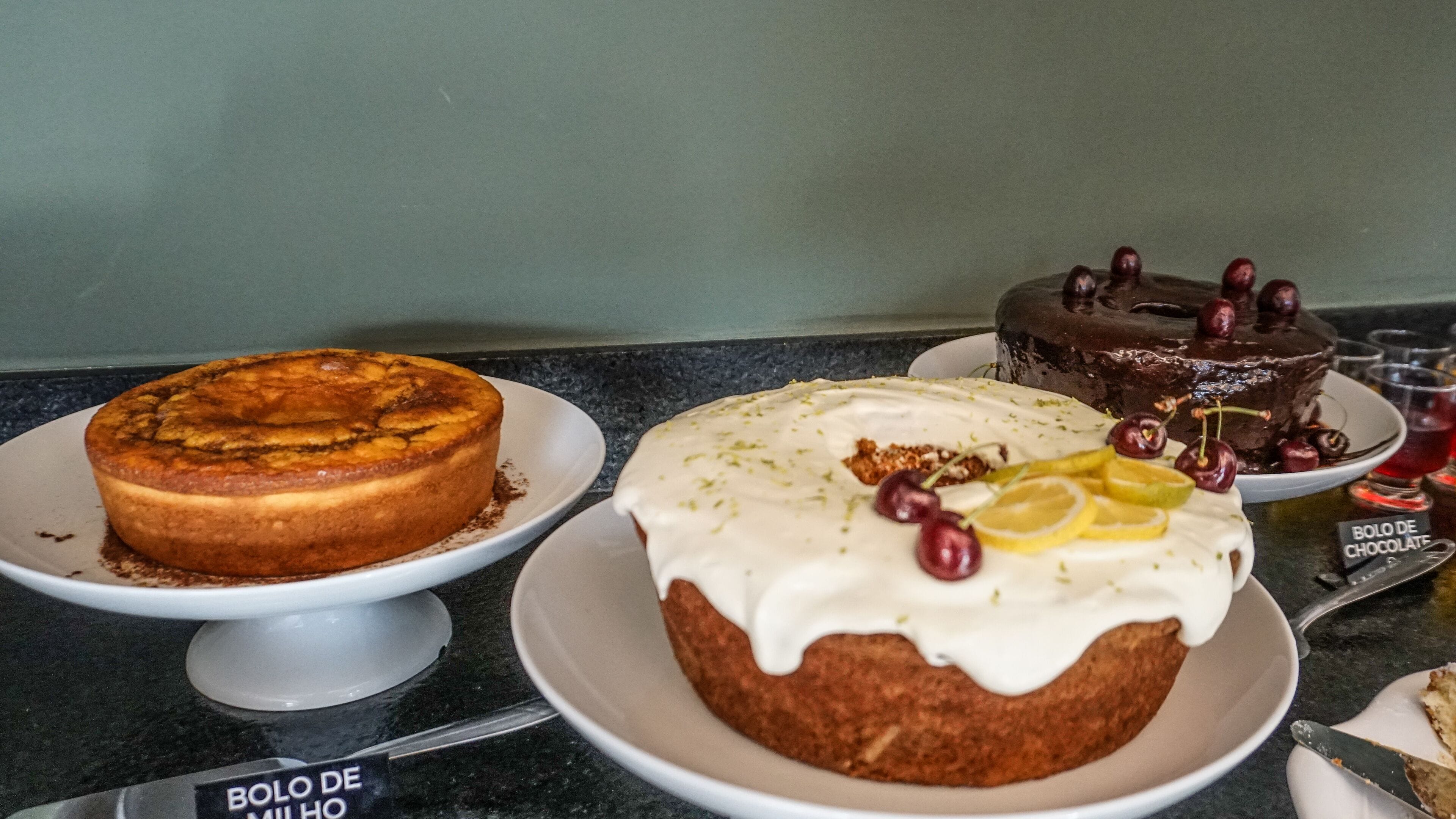 Three cakes on white plates on a black countertop.