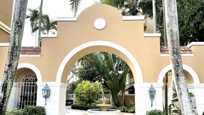 A gated entrance with a central archway, surrounded by trimmed hedges and palm trees. - Yacht Club Miami Suite 2 Bedroom and 2 Bathroom With Baby Crib & Free Parking (Aventura)