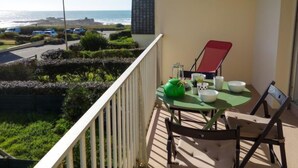 Ein Balkon mit Tisch für Zwei, Blick auf eine Küstenstraße mit parkenden Autos und Meerblick.