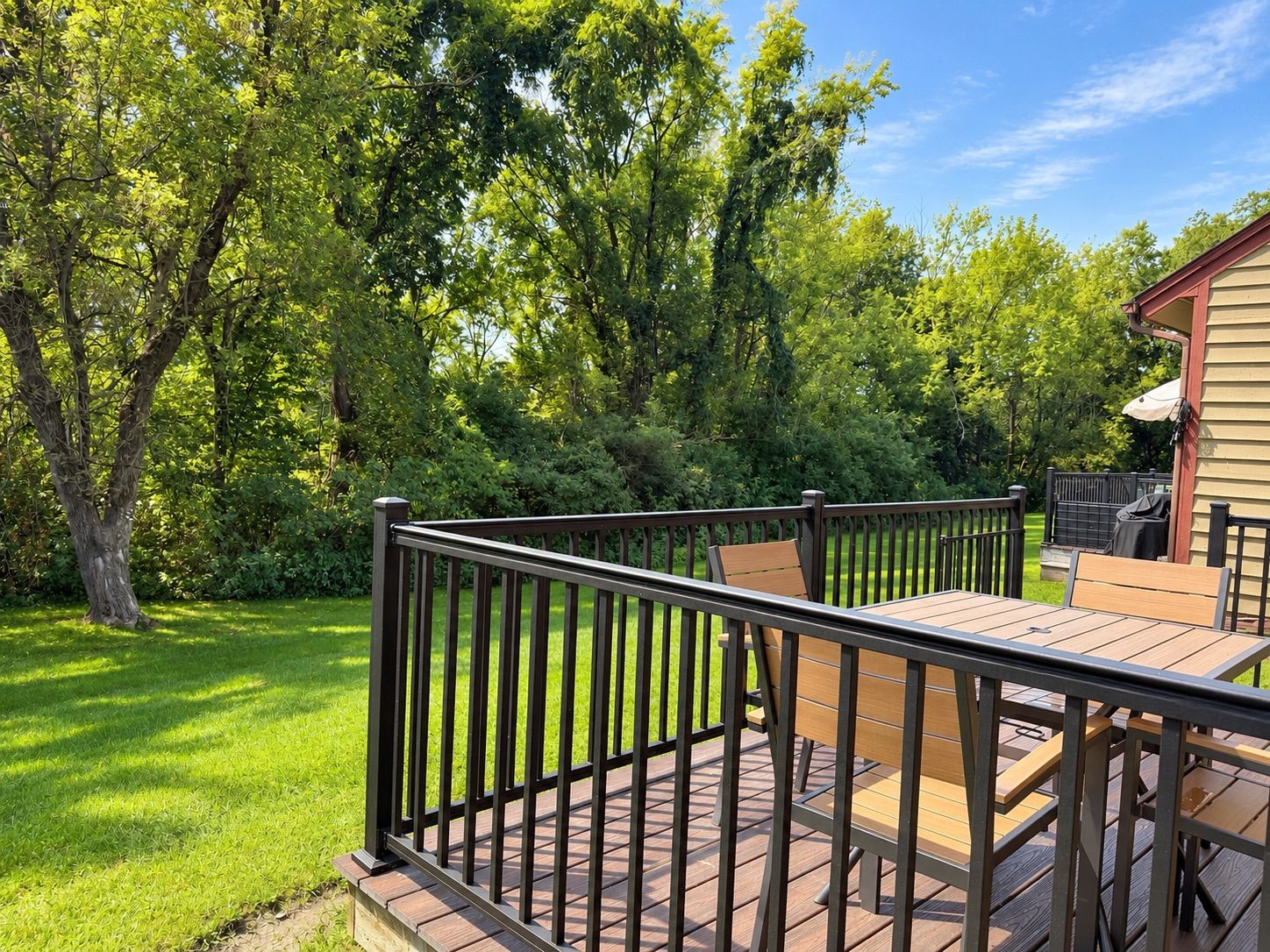 Une terrasse dotée d’une rambarde en métal, entourée d’une végétation luxuriante et d’arbres.