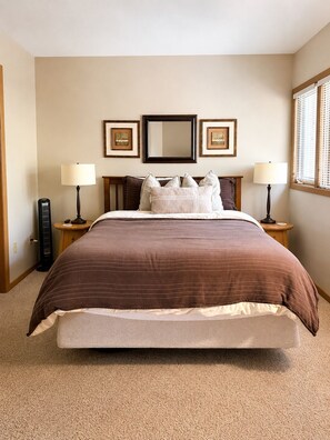 A bedroom with a large bed, two bedside lamps, a heater, and three framed pictures on the wall. - Fall Galena Getaway - Private Deck + Resort Access (Galena)