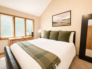 A bedroom with a large bed, a bedside table, a lamp, a window with blinds, and a painting on the wall. - Cozy Galena Getaway: Fireplace + Resort Access (Galena)