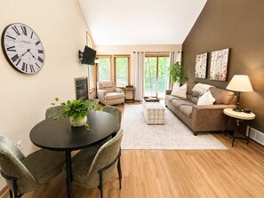 A modern living room with a round table, two armchairs, a sofa, a TV mounted on the wall, and a large wall clock. - Cozy Galena Getaway: Fireplace + Resort Access (Galena)