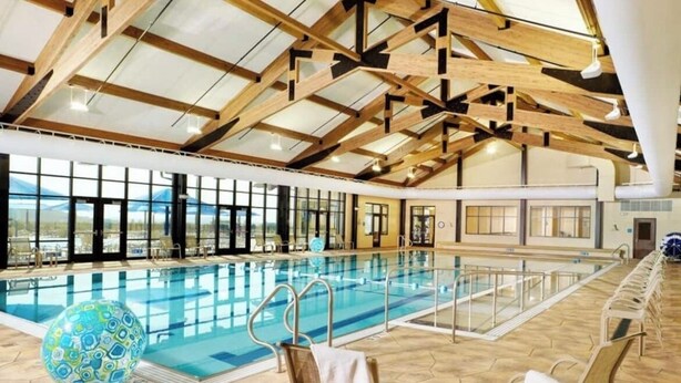 Piscina interna com teto alto e vigas de madeira, cercada por espreguiçadeiras e uma grande bola decorativa.