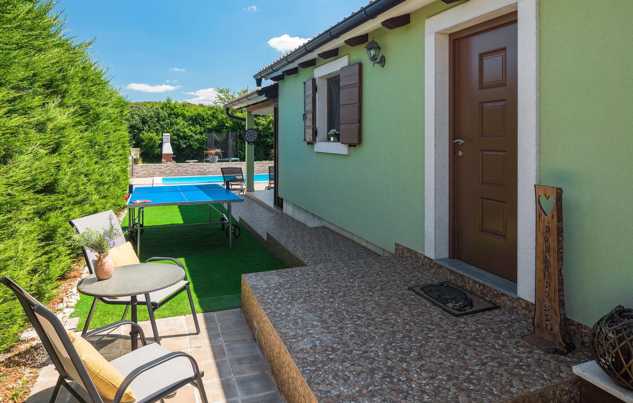 A house with a green exterior, a pool, and outdoor seating.