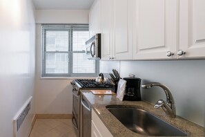 A kitchen with white cabinets, a stainless steel sink, a stove, and a window with blinds.
